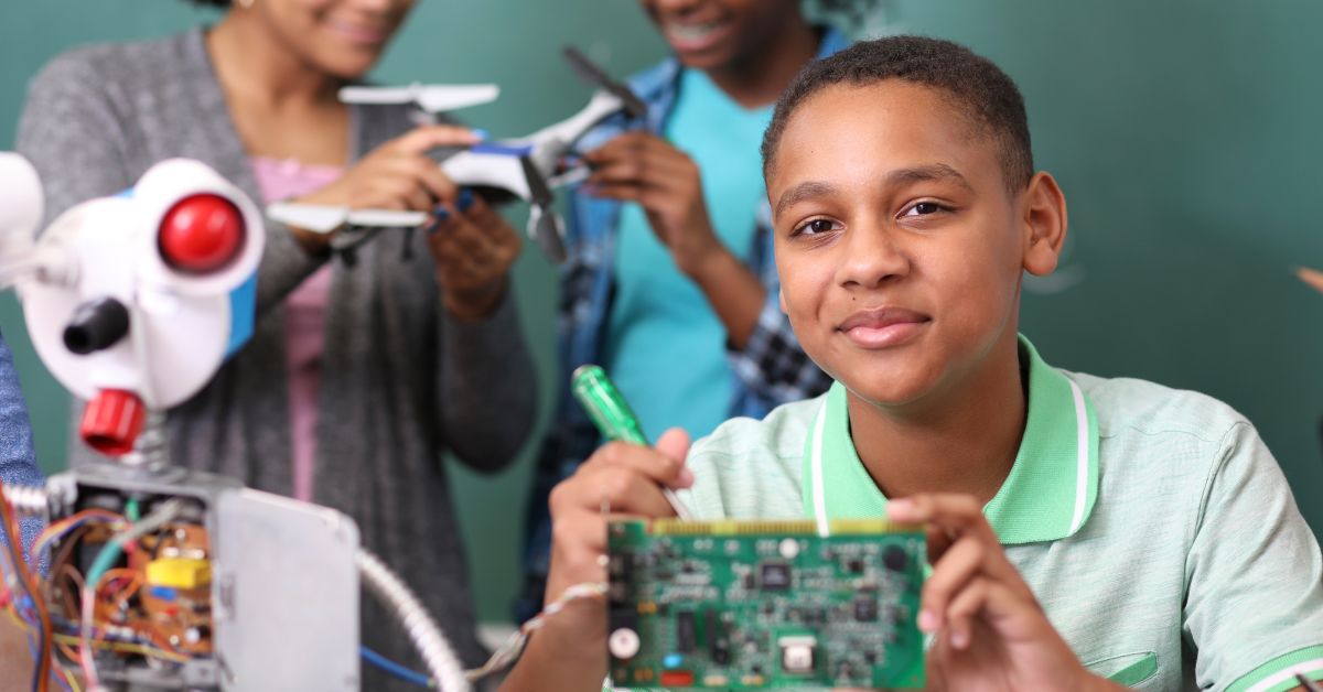 Young Black male student working with a circuit board, two Black female students in the background